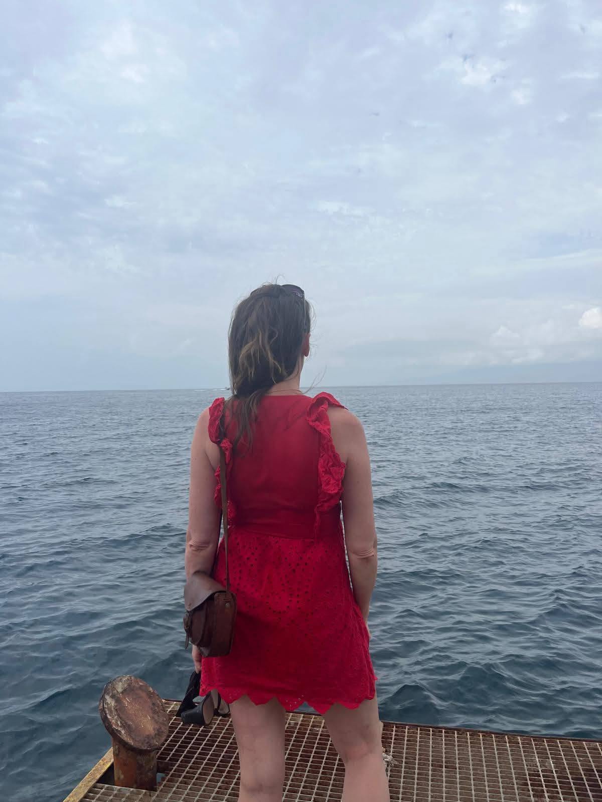 Une femme en robe rouge, vue de dos face à la mer, illustration d’un article sur le voyage comme ressource de transformation.