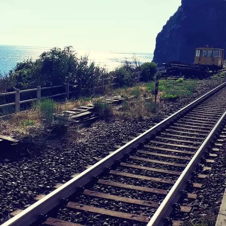 Voie ferrée longeant la mer avec un petit train au loin.