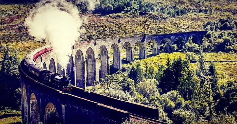 Train à vapeur traversant un grand viaduc dans un paysage vallonné.